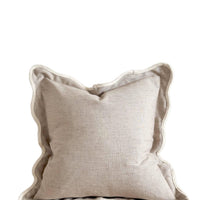 Beige pillow with ruffled edge on a wooden surface against a white wall