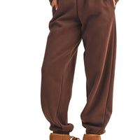 Brown sweatpants worn with brown platform boots on a beige background