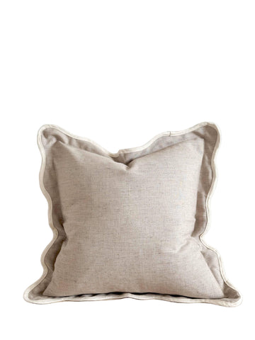 Beige pillow with ruffled edge on a wooden surface against a white wall