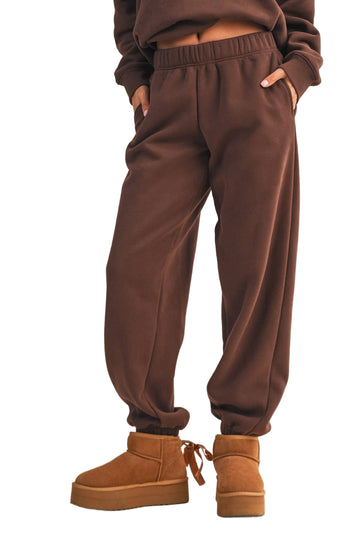 Brown sweatpants worn with brown platform boots on a beige background