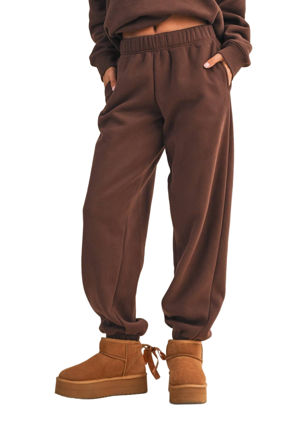 Brown sweatpants worn with brown platform boots on a beige background