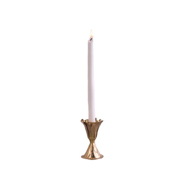 Gold candle holder with a lit white candle on a gray surface and light gray background