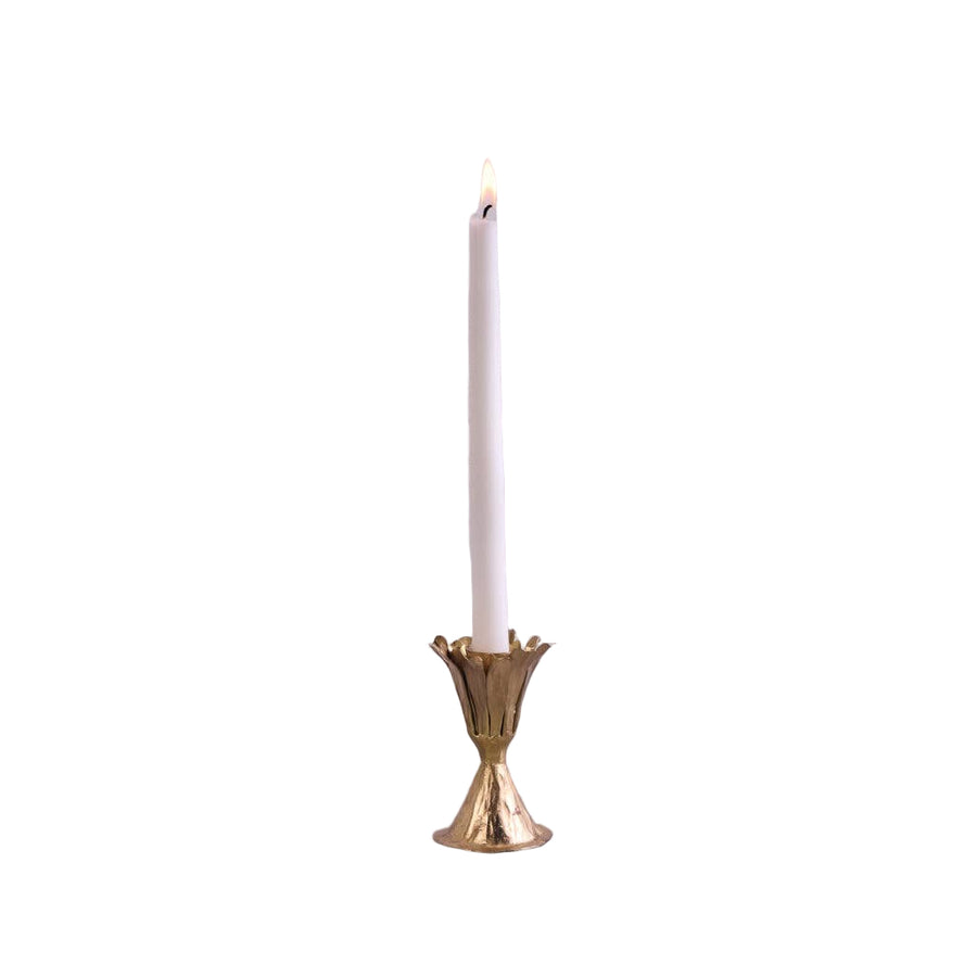 Gold candle holder with a lit white candle on a gray surface and light gray background